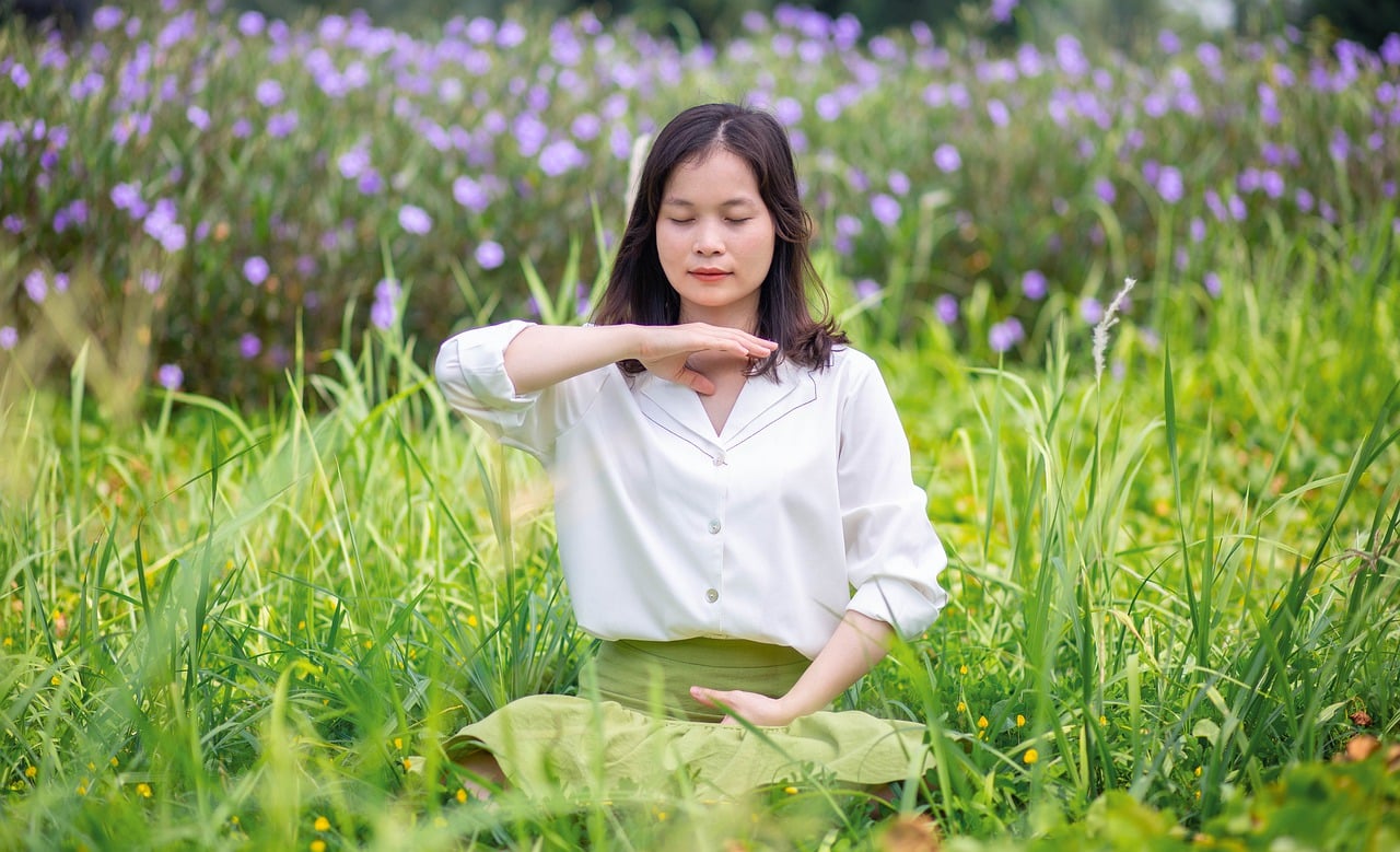 A woman gracefully practices meditation amidst a picturesque field of vibrant purple flowers, embodying serenity and balance in nature. Her tranquil posture exudes a sense of peace and mindfulness, symbolizing the journey towards equilibrium and relief from Meniere's Disease through holistic approaches